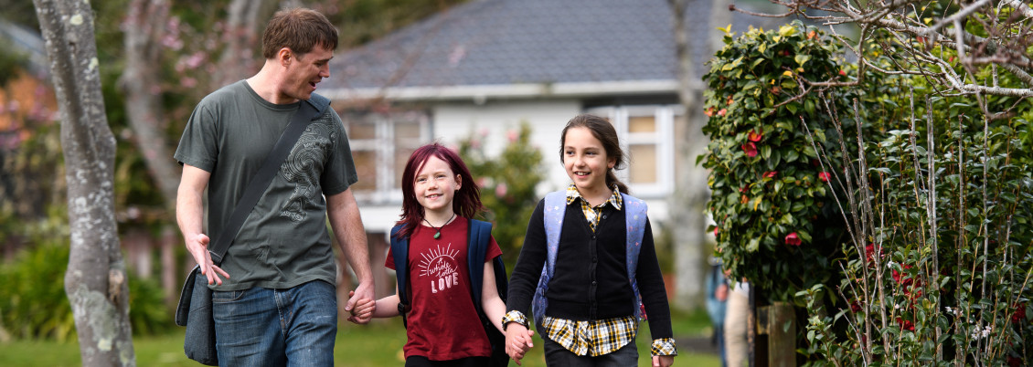 Two smiling children hold hands with their dad as they walk to school